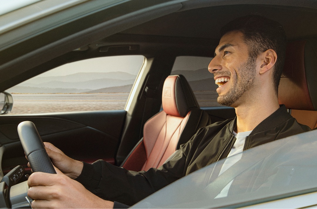 Man drives the 2022 RX F Sport, he is smiling and both hands are on the steering wheel. Mountains can be seen in the far distance through the passenger window.